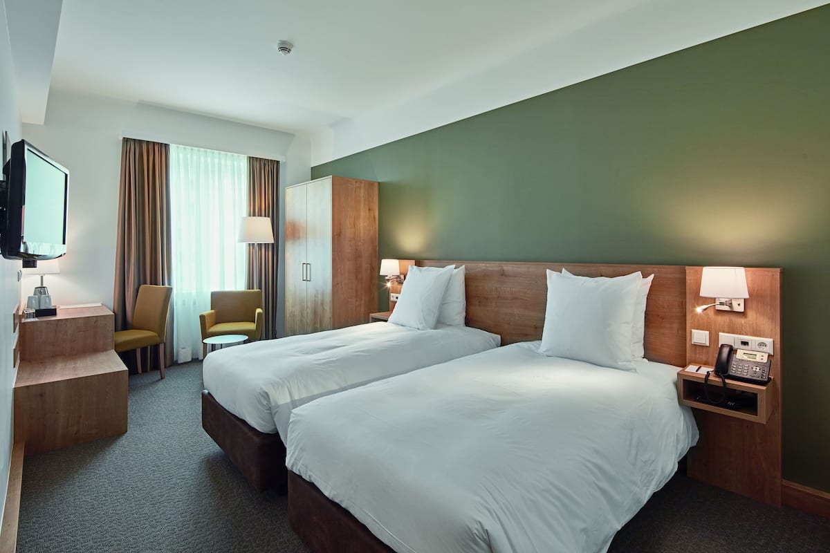 Ein Hotelzimmer mit zwei Betten, einem Schreibtisch mit Lampe, einem Stuhl und einem Fernseher.