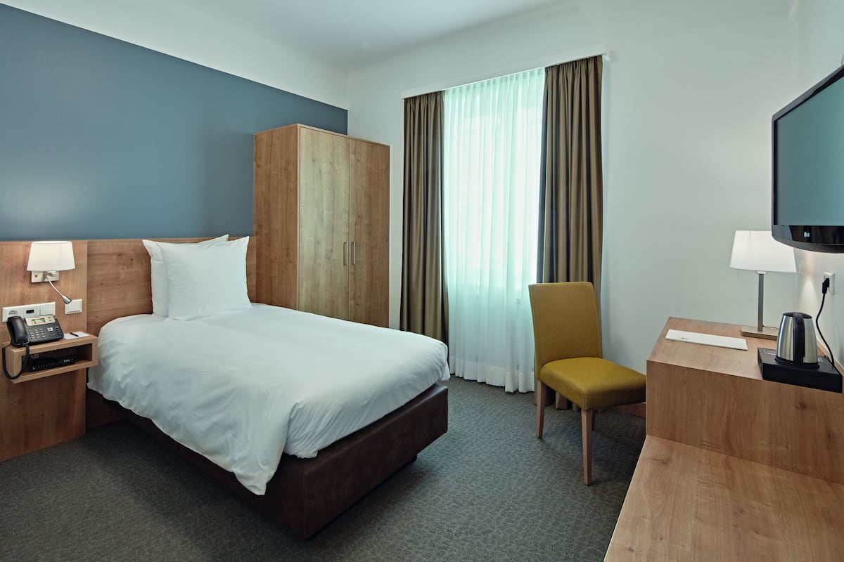 Ein Hotelzimmer mit Bett, Holzschrank, Schreibtisch mit Stuhl, Fernseher und Telefon.