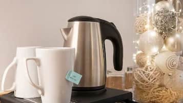 A stainless steel kettle on a black tray, two white mugs, and a decorative glass container with white ornaments.