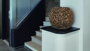 A modern interior with a curved staircase, a reception desk, and a large decorative sculpture. - City Hotel (Luxembourg City)