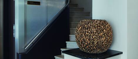 Un interior moderno con una escalera curva, un mostrador de recepción y una gran escultura decorativa.