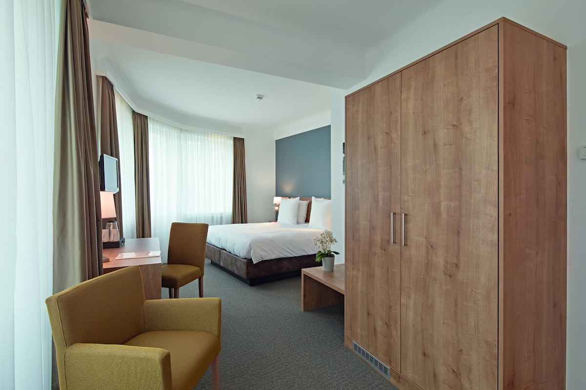 Ein Hotelzimmer mit einem Bett, einem Schrank, einem Schreibtisch mit Stuhl und einem kleinen Tisch.