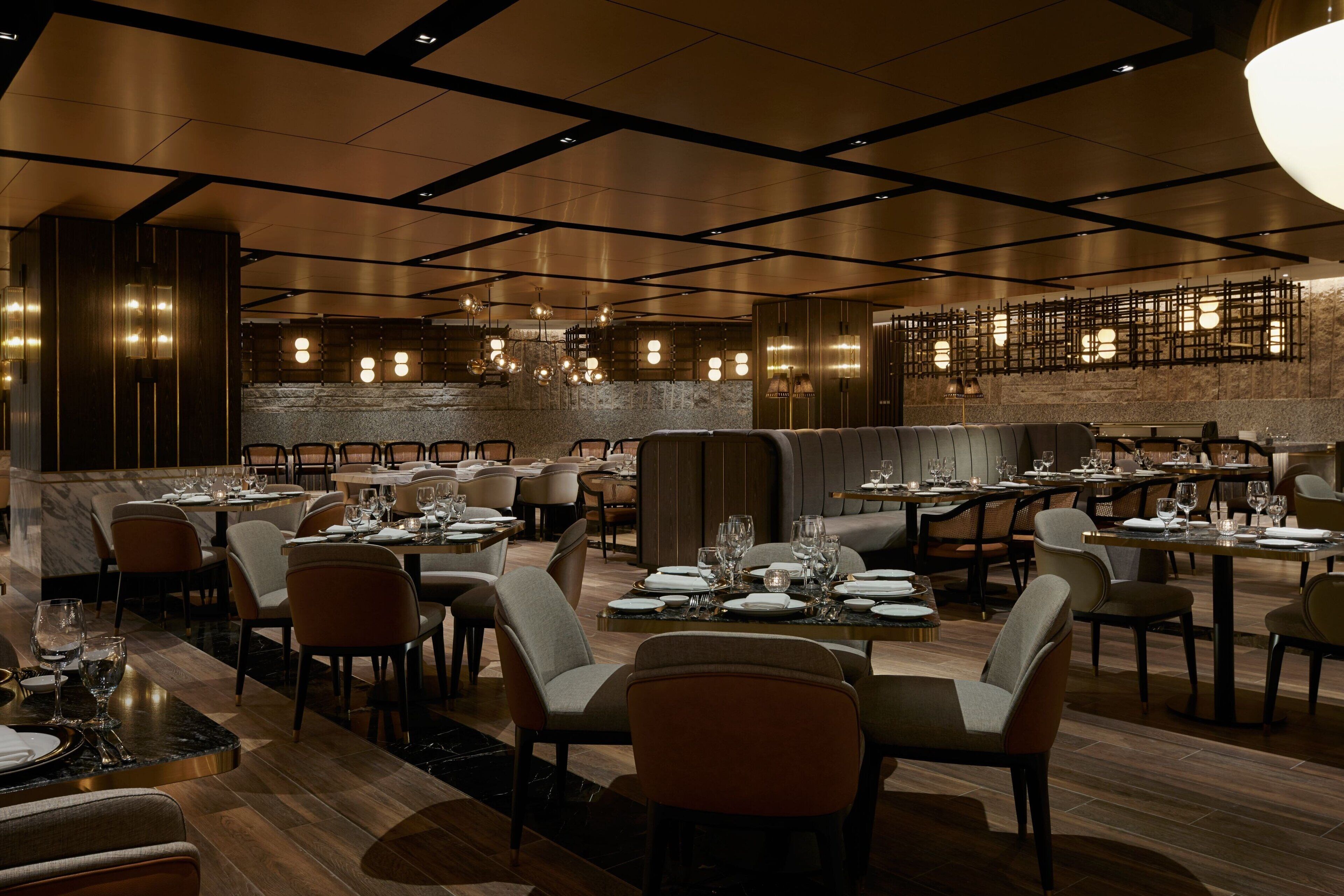 Un'ampia sala ristorante con diversi tavoli e sedie, un moderno design del soffitto e un muro in pietra sullo sfondo.