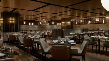 Un'ampia sala ristorante con diversi tavoli e sedie, un moderno design del soffitto e un muro in pietra sullo sfondo.