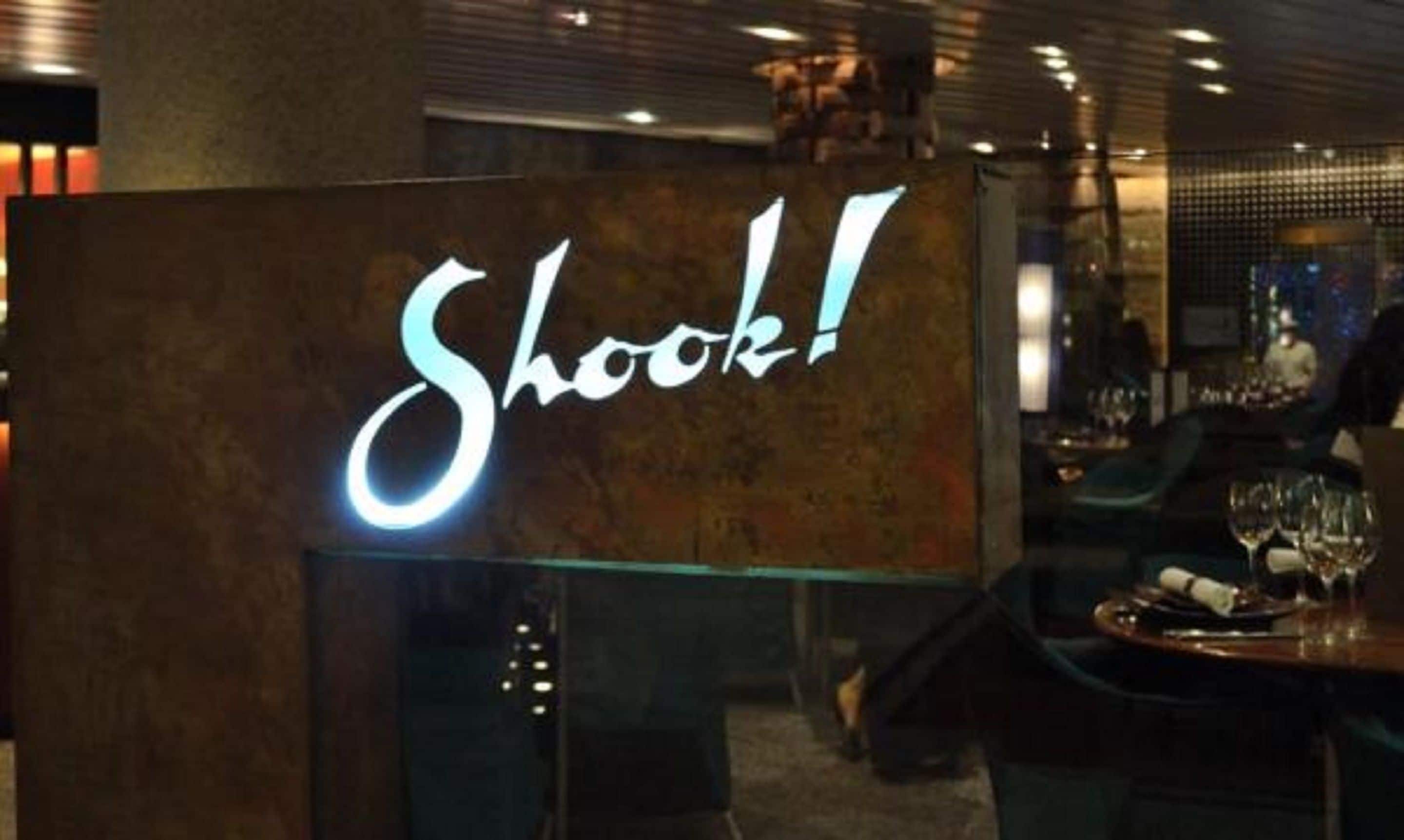 A bar area with a neon sign that reads "Shook!"