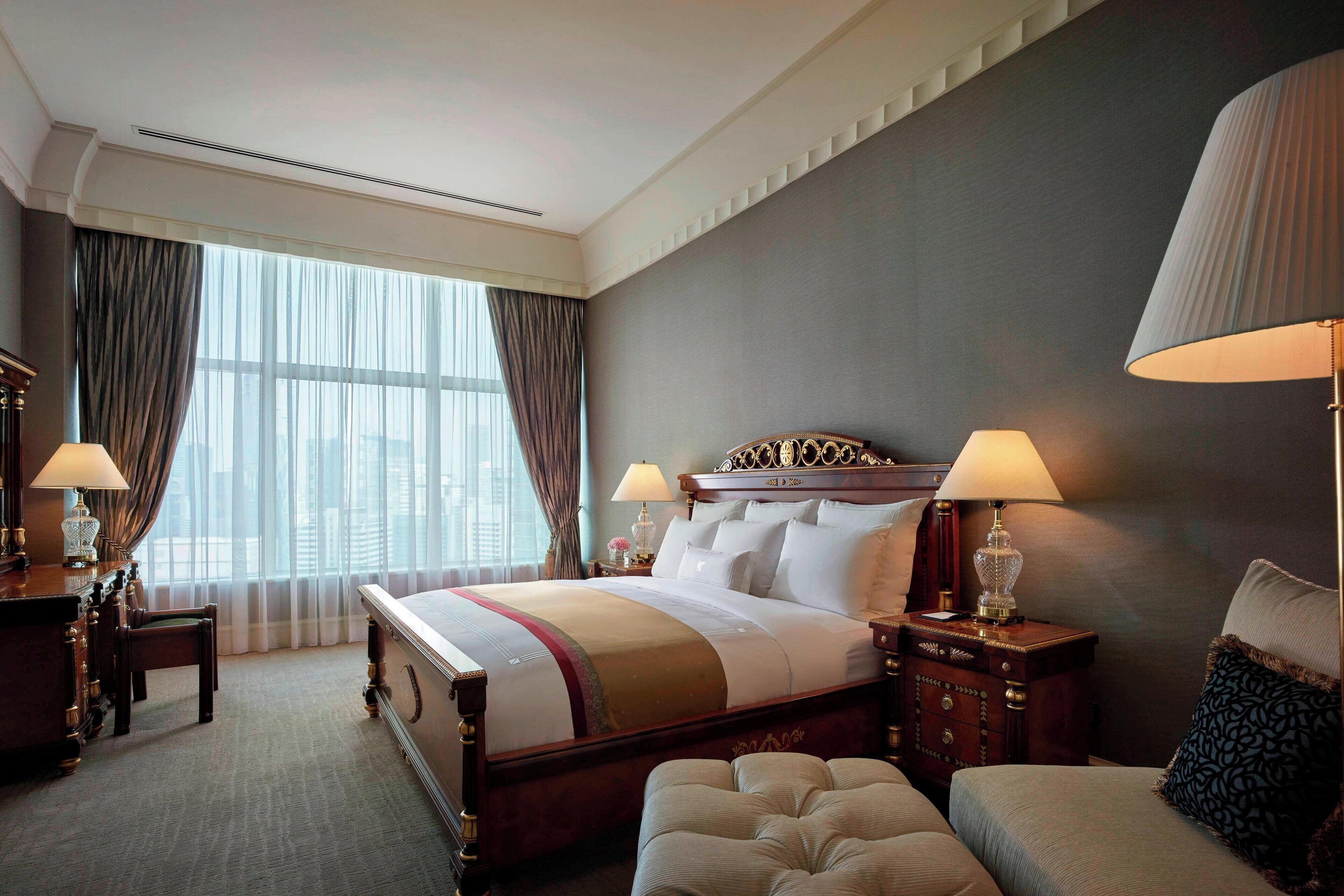 A hotel room with a large bed, two bedside tables with lamps, a chair, and a window with curtains.