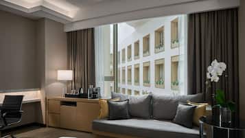 A hotel room with a sofa, a desk, a chair, a lamp, and a window with curtains.