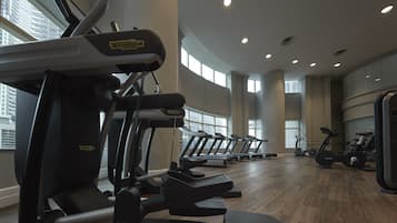 A gym with multiple treadmills and elliptical machines, large windows, and a high ceiling.