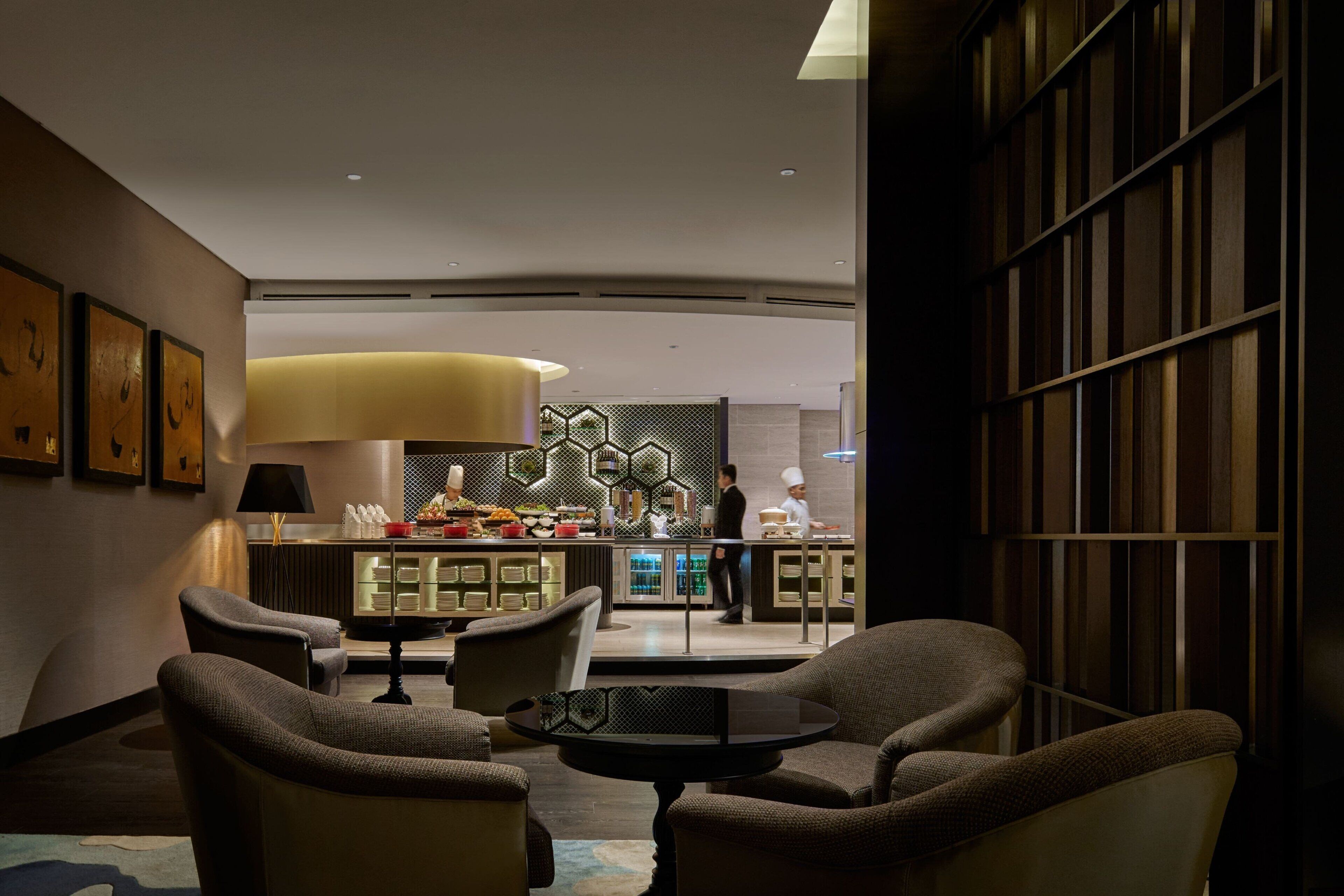 Een moderne lobby met comfortabele zitplaatsen, een centrale tafel en een bar op de achtergrond.