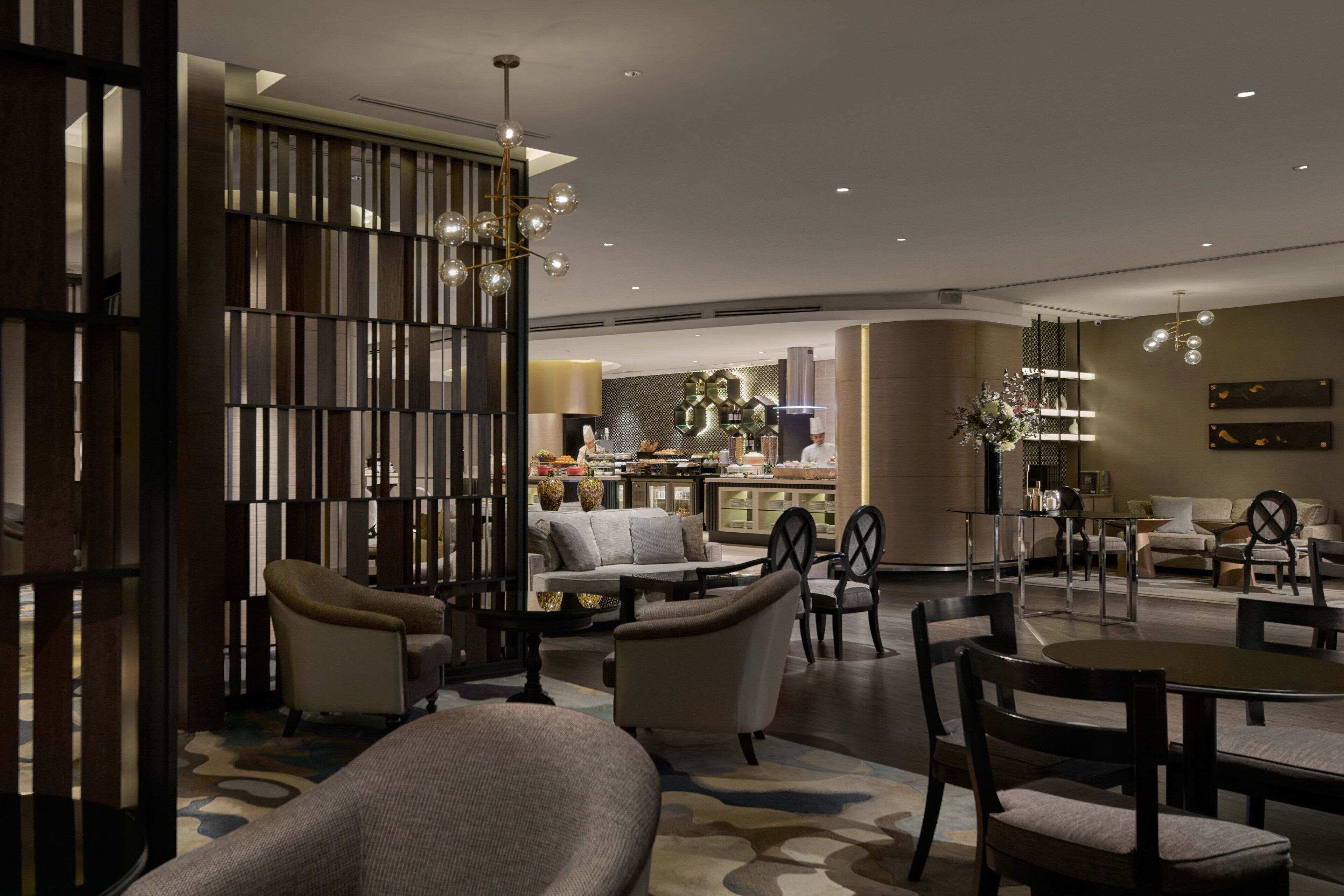 A modern hotel lobby with a seating area, a bar, and a kitchen in the background.