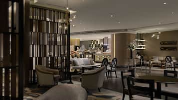 A modern hotel lobby with a seating area, a bar, and a kitchen in the background.