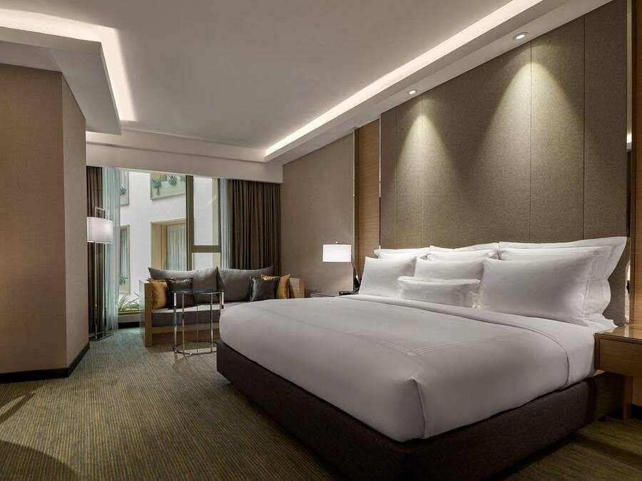 A modern hotel room with a large bed, a desk with a lamp, a sofa, and a view of the outside.
