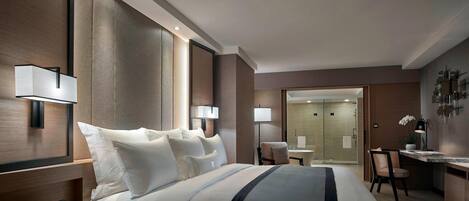 A modern hotel room with a large bed, bedside lamps, a desk, and a bathroom visible through an open door.