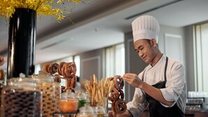 A chef preparing food in a modern kitchen with a large vase of yellow flowers, various food items on the counter, and a window in the background. - JW Marriott Kuala Lumpur (Kuala Lumpur)