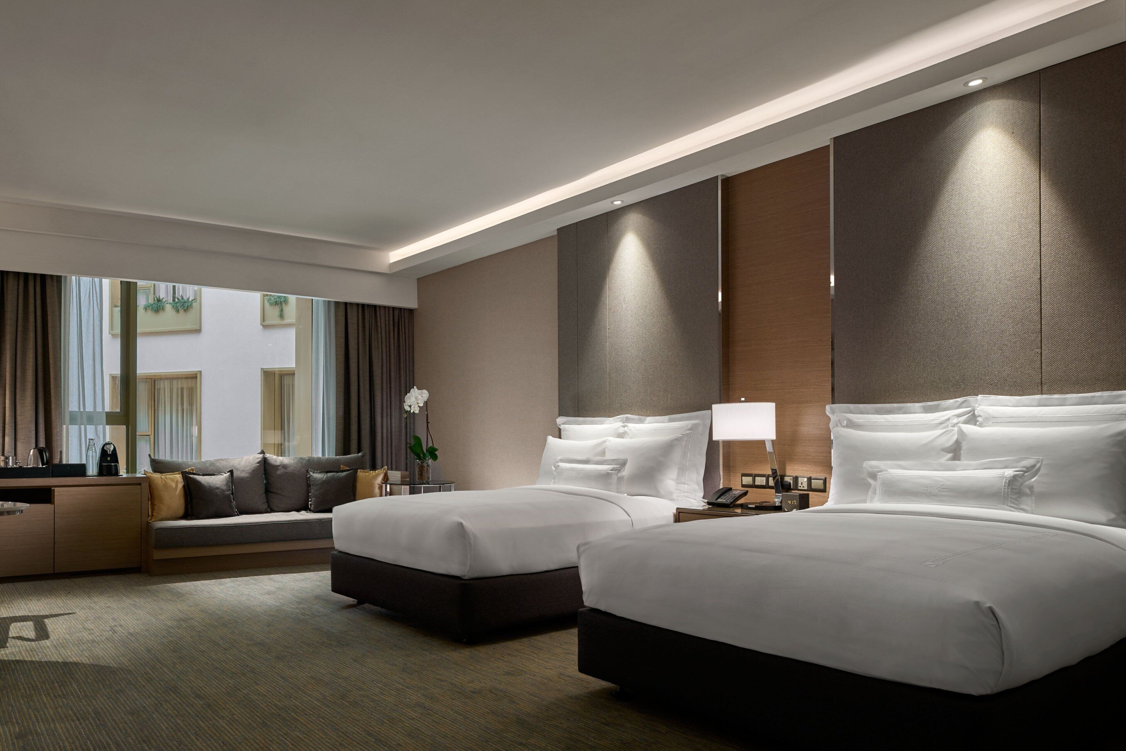 A hotel room with two beds, a sofa, a desk, and a large window with curtains.
