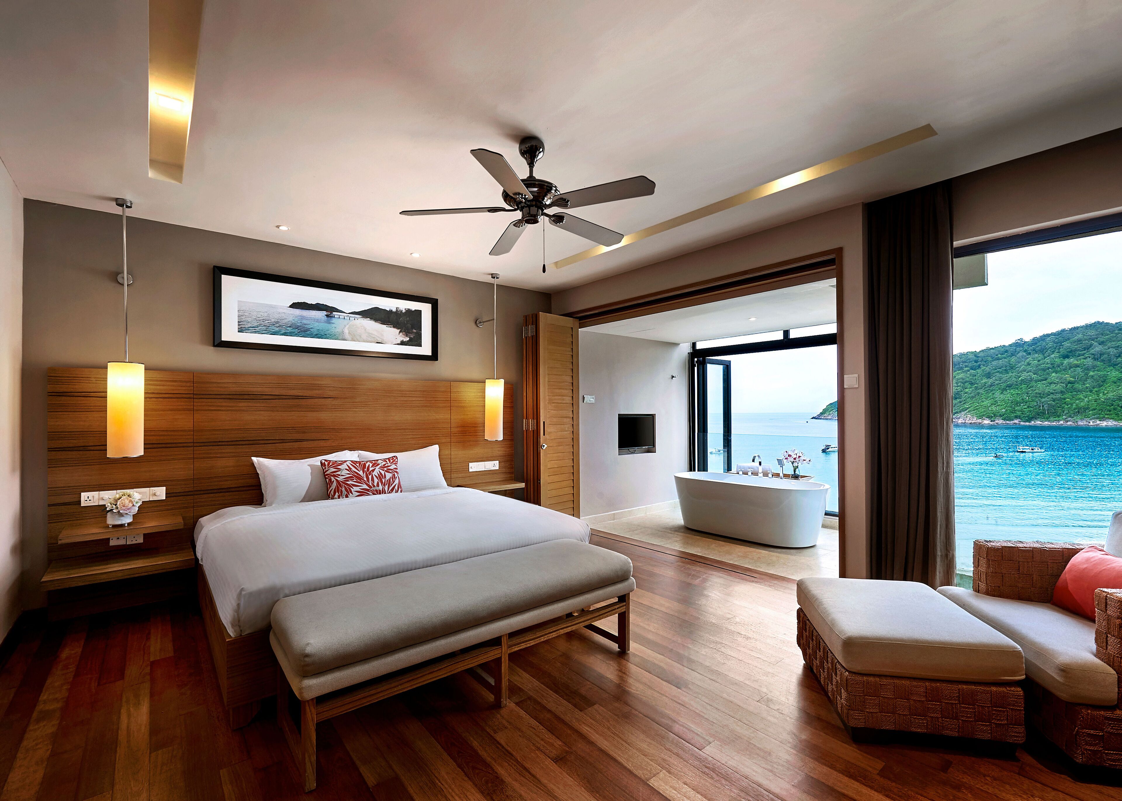 A modern hotel room with a large bed, a ceiling fan, a bathtub, and a view of the sea.