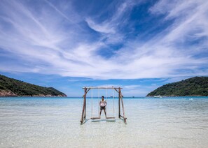 A wooden swing set in clear shallow water with a person on it, surrounded by a calm sea and distant hills. - The Taaras Beach & Spa Resort (Redang Island)