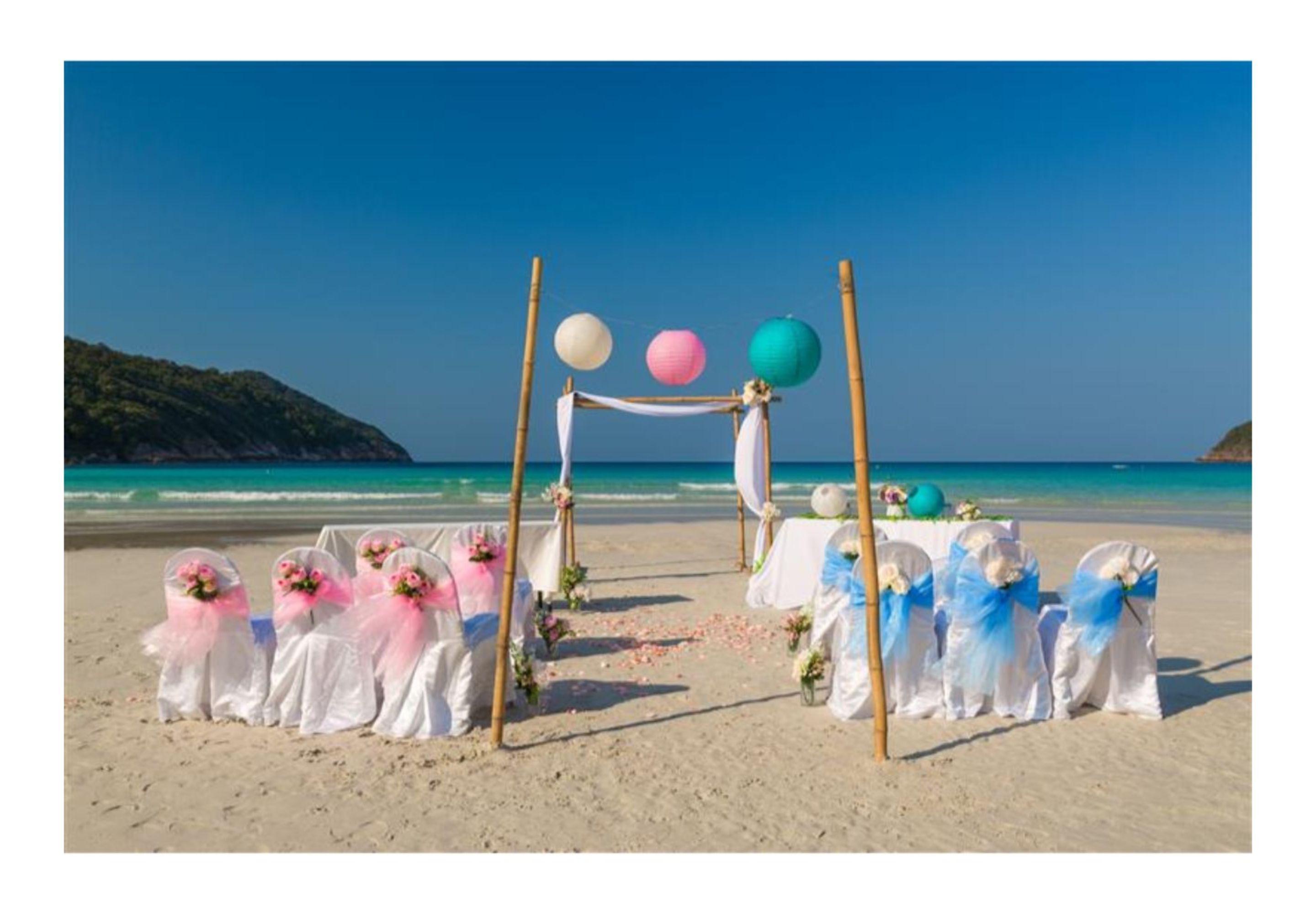 A beach wedding setup with white and blue chairs, a white arch, and balloons.