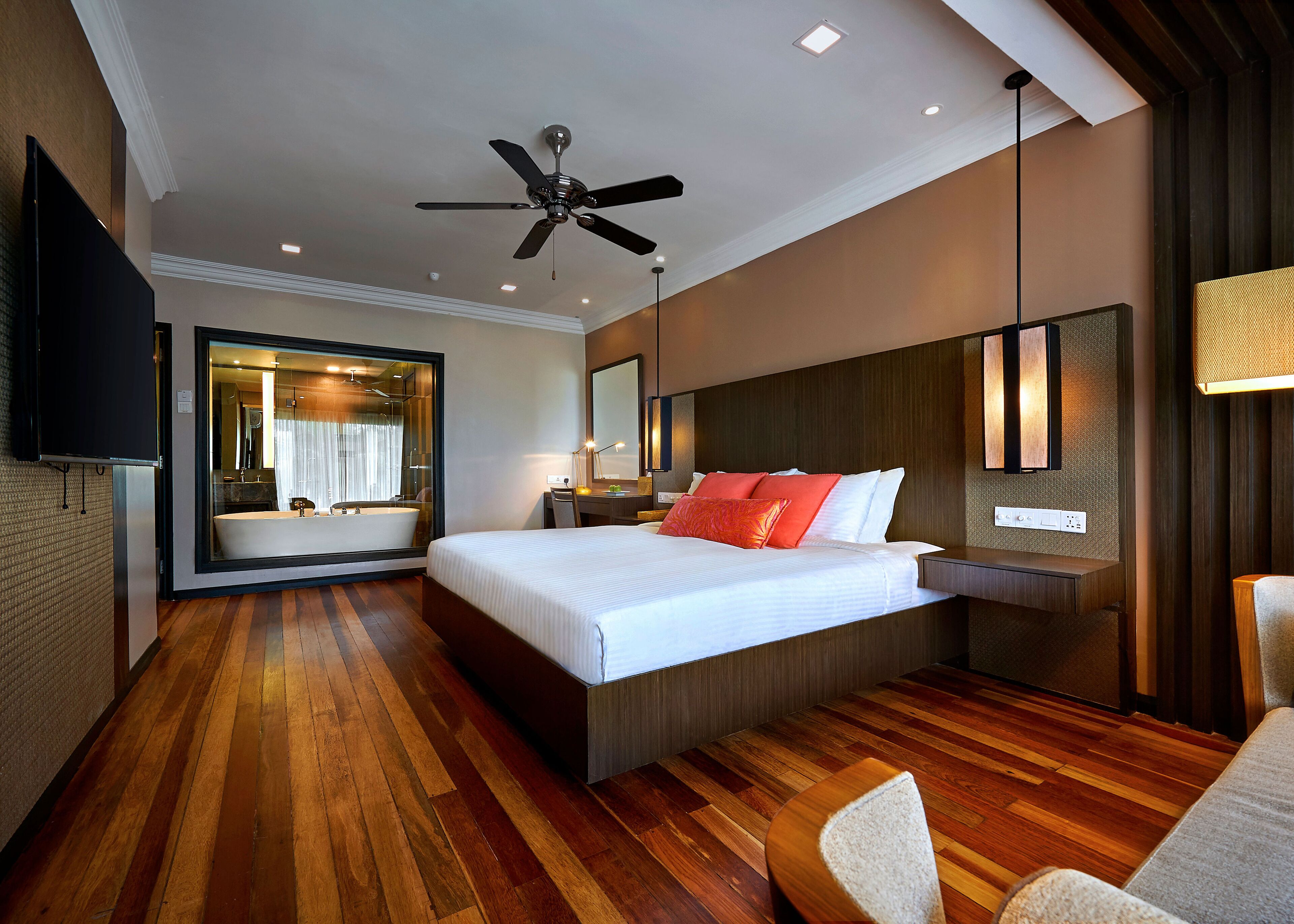 A modern hotel room with a large bed, a ceiling fan, a bathroom with a bathtub, and a TV mounted on the wall.