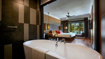 A modern bathroom with a large bathtub, a visible towel, and a view of a bedroom with a bed and a window.