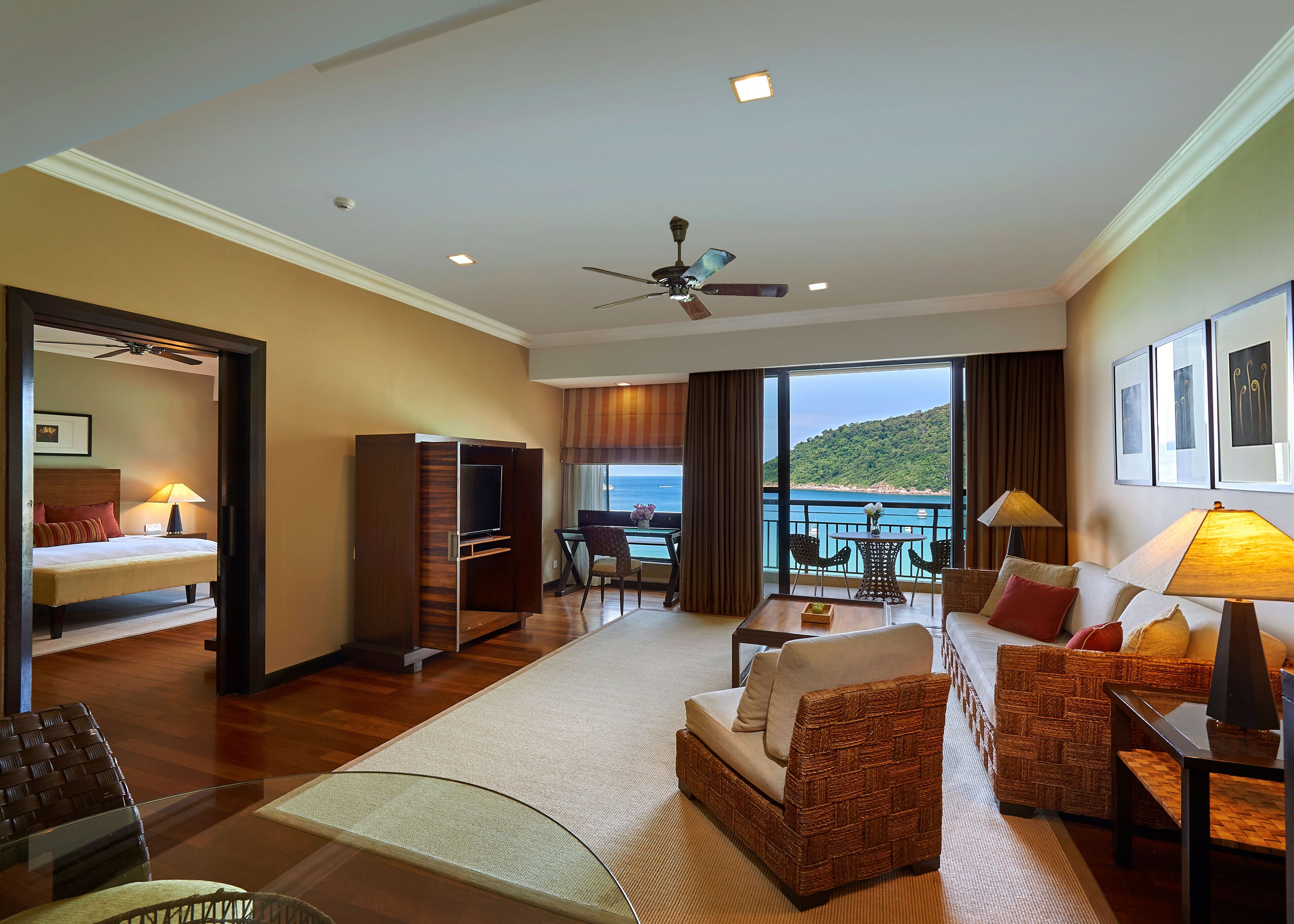 A hotel room with a bed, a TV, a balcony with a table and chairs, and a view of the sea.