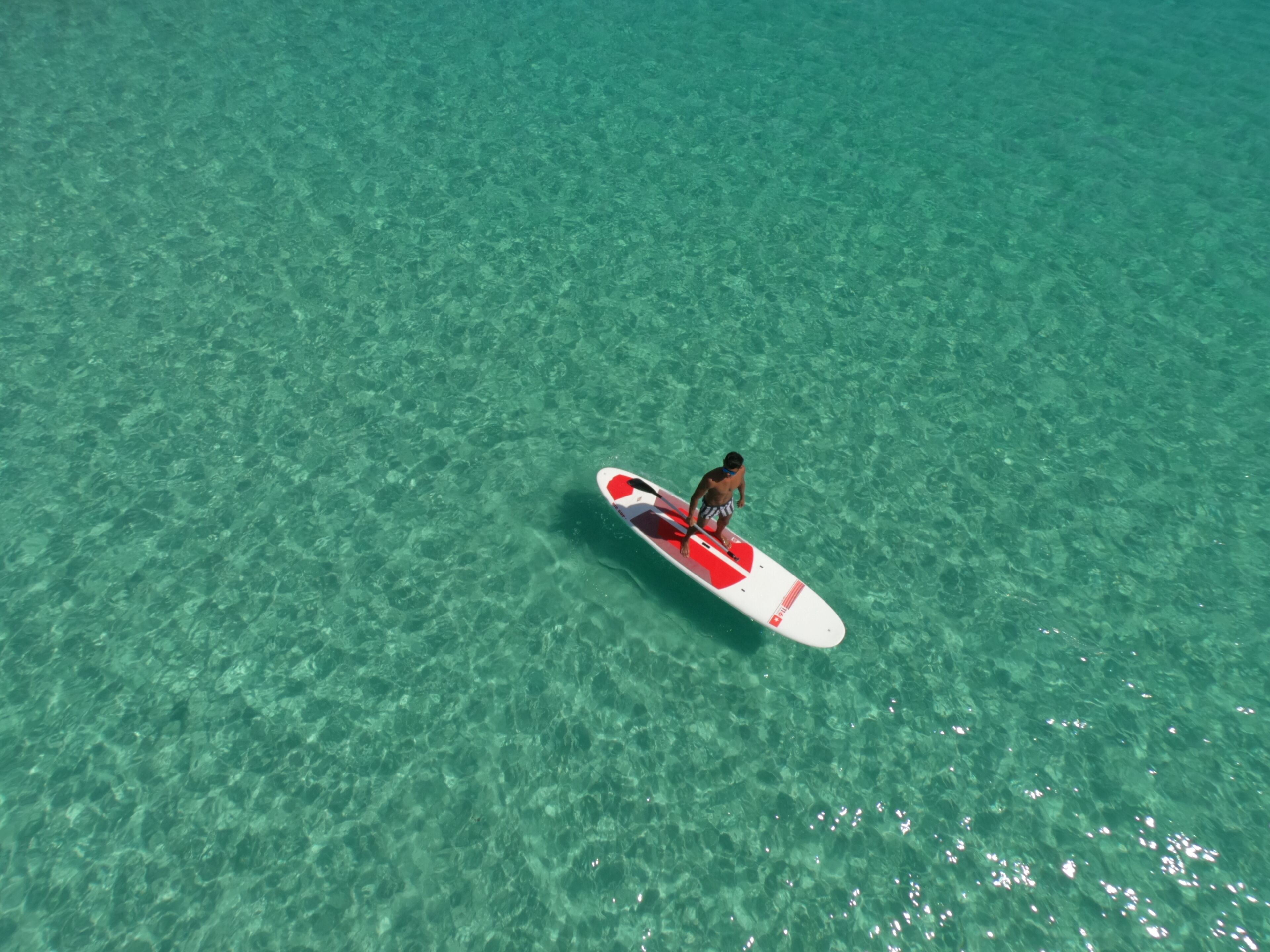 A person standing on a surfboard in clear turquoise water.
