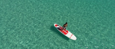 A person standing on a surfboard in clear turquoise water.