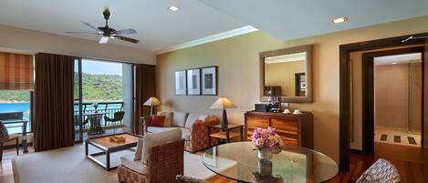 A spacious living area with a glass coffee table, wicker furniture, a sofa, and a balcony with a view of the sea.