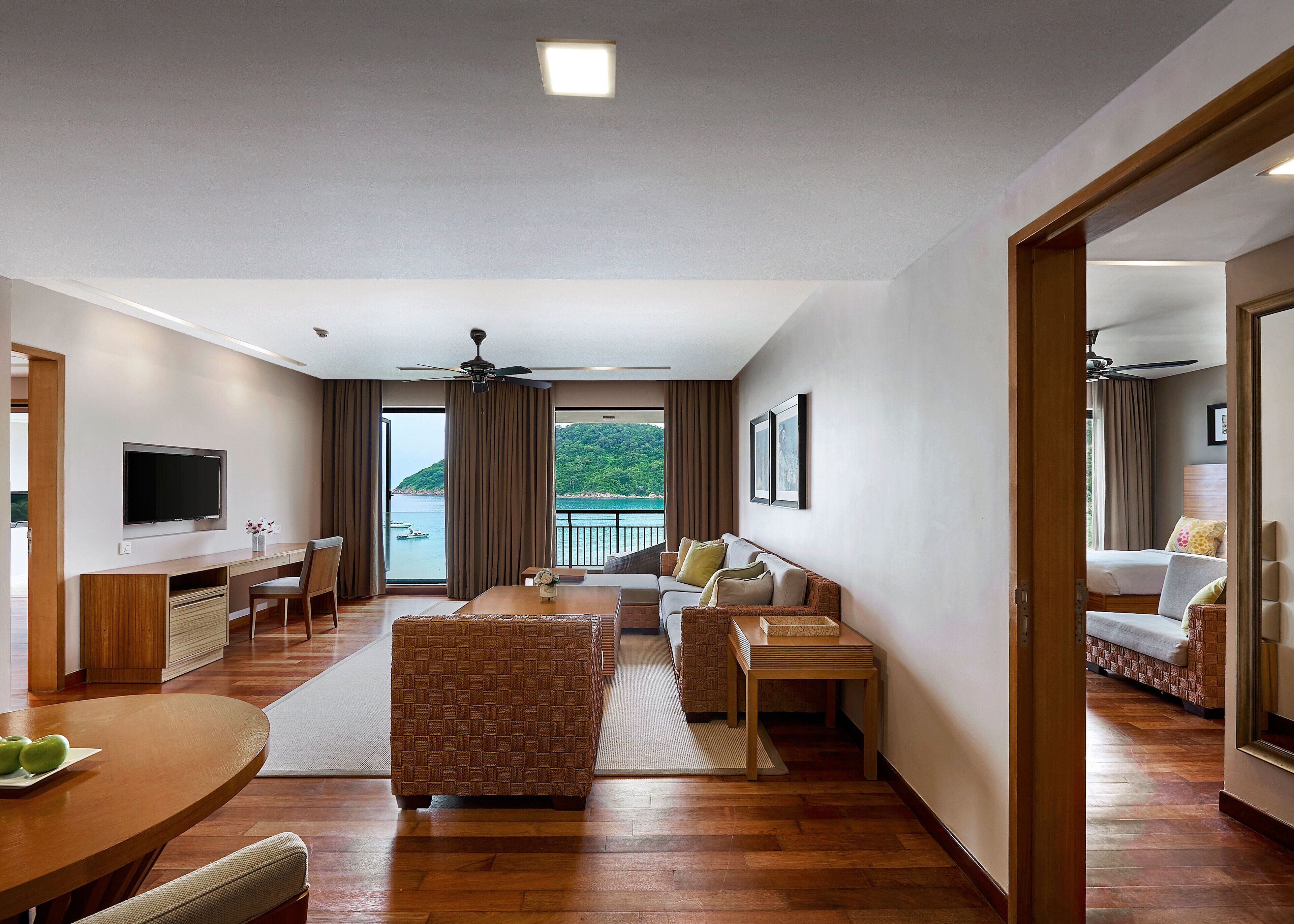A modern hotel room with a balcony, a flat-screen TV, a dining area, and a cozy seating space.