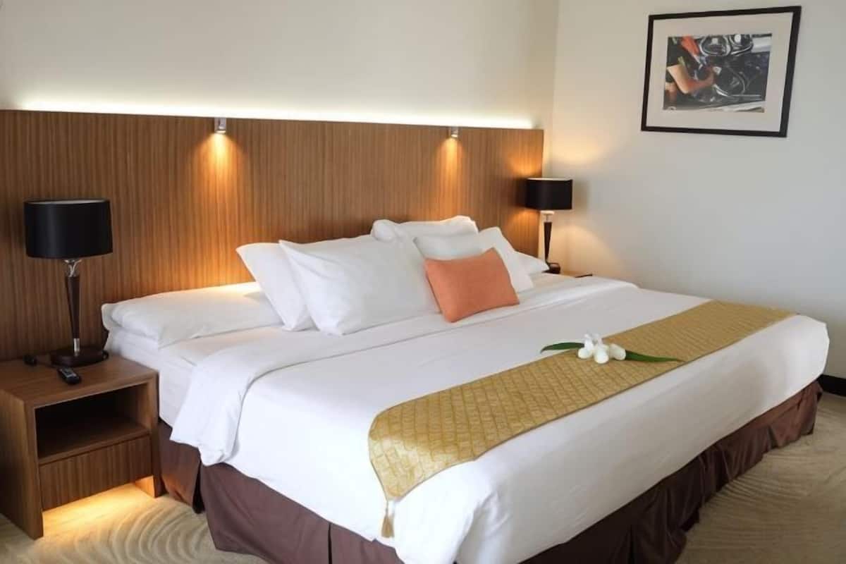 Une chambre d’hôtel avec un lit, des tables de chevet, des lampes, un tableau encadré au mur et une plante décorative.