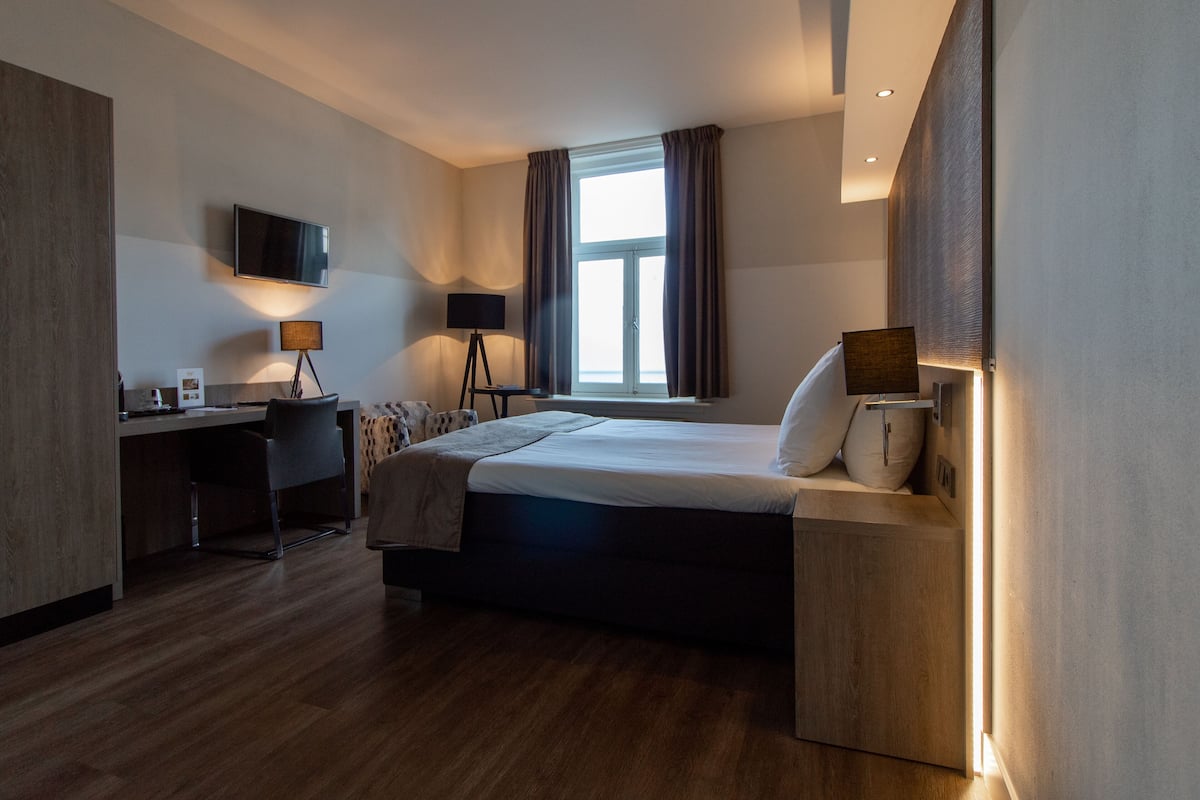 A modern hotel room with a bed, desk, and a large window with curtains.