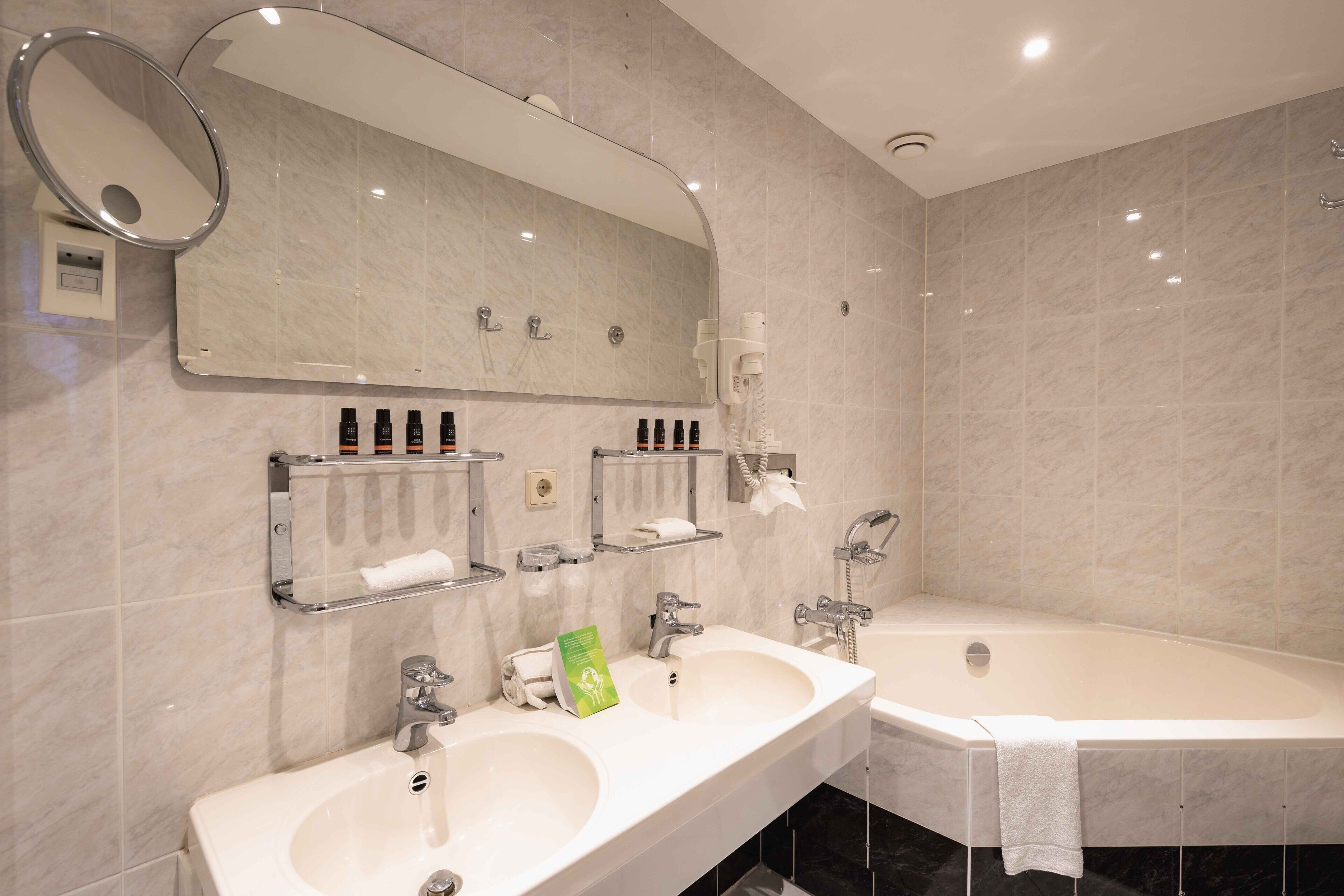 A modern bathroom with two sinks, a large mirror, and a bathtub.