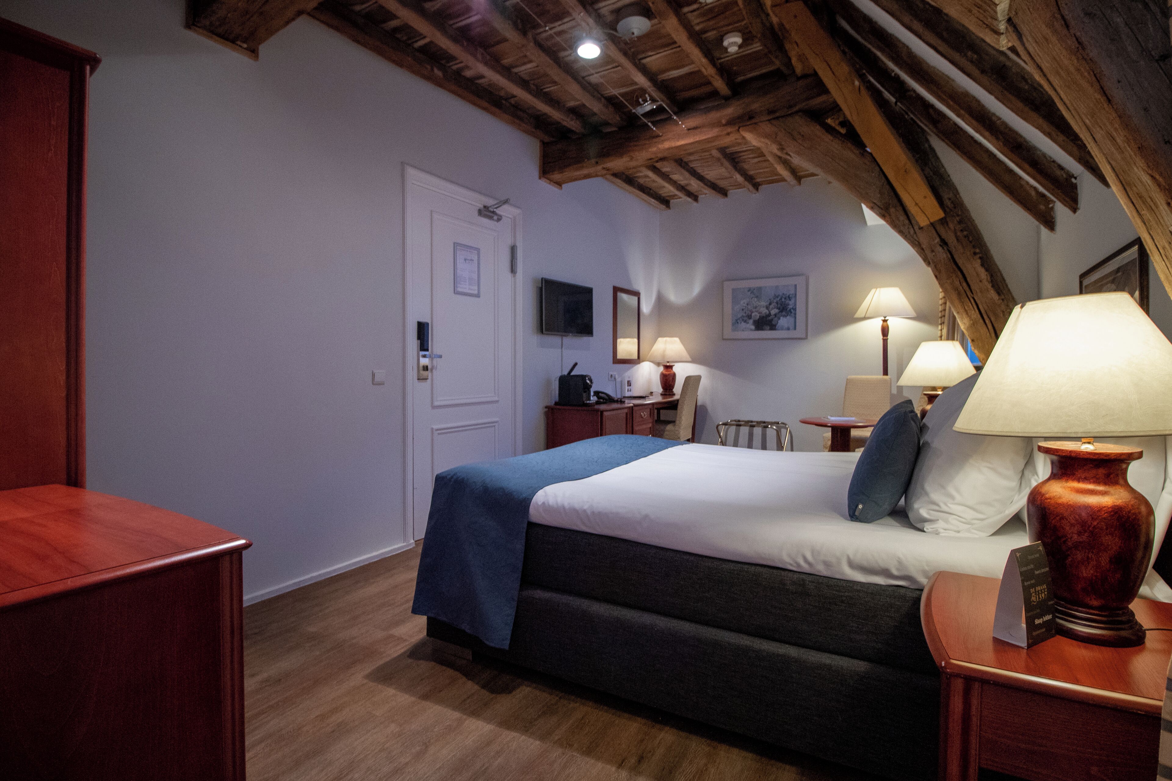 Un dormitorio con cama, mesitas de noche, un escritorio, una silla y techo de madera.