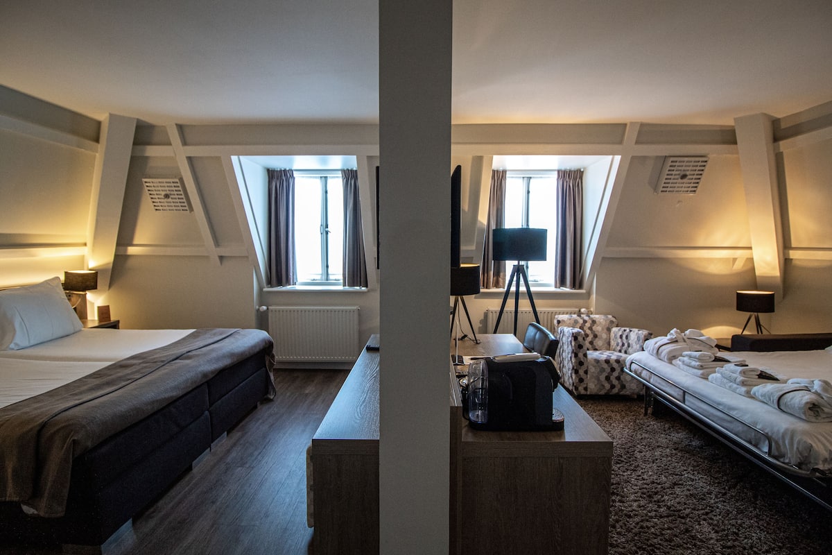 A hotel room with a large bed, a desk, a chair, and a TV on a tripod.