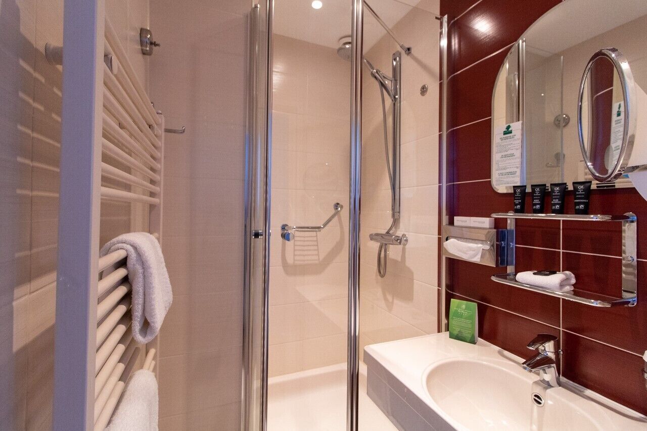A modern bathroom with a glass-enclosed shower, a white sink, and a vanity with a mirror and toiletries.