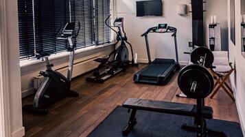 A home gym with exercise equipment including a treadmill, elliptical, stationary bike, and a bench with weights.