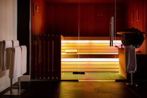 A sauna with wooden walls and a bench. There are towels on a rack to the left.