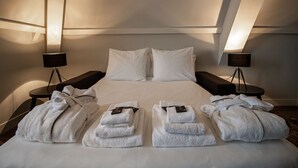 A neatly made bed with white linens and pillows, two bedside tables with lamps, and four folded towels on the bed.