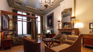 A spacious hotel room with a large bed, a sitting area with chairs, a desk, and a fireplace.