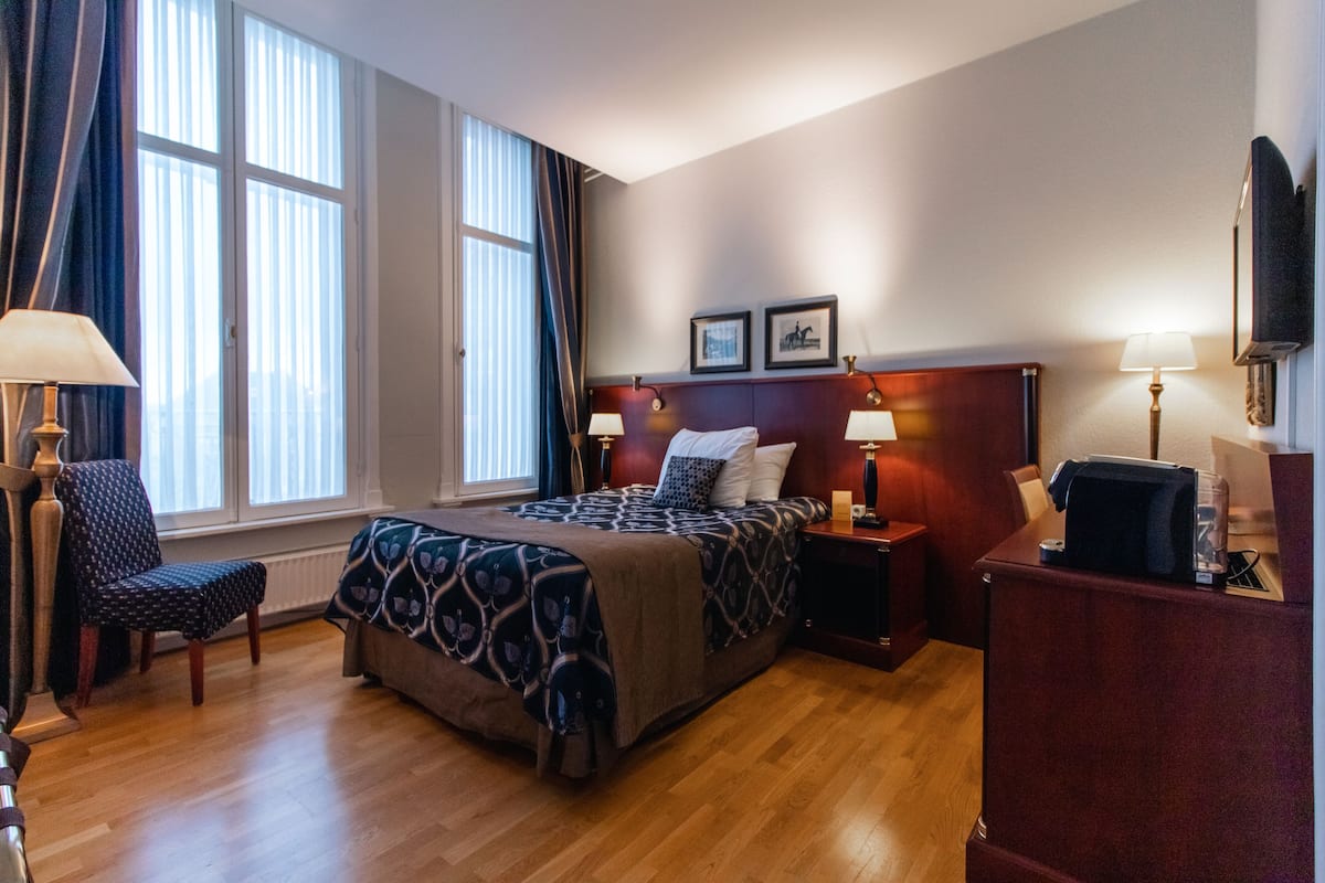 A hotel room with a large bed, two bedside tables, a chair, a desk, and a TV.