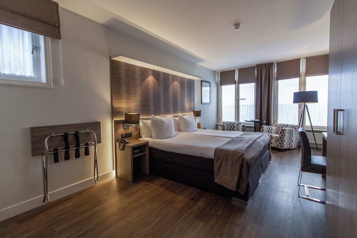 A hotel room with a large bed, bedside tables, a chair, a desk, and a lamp.