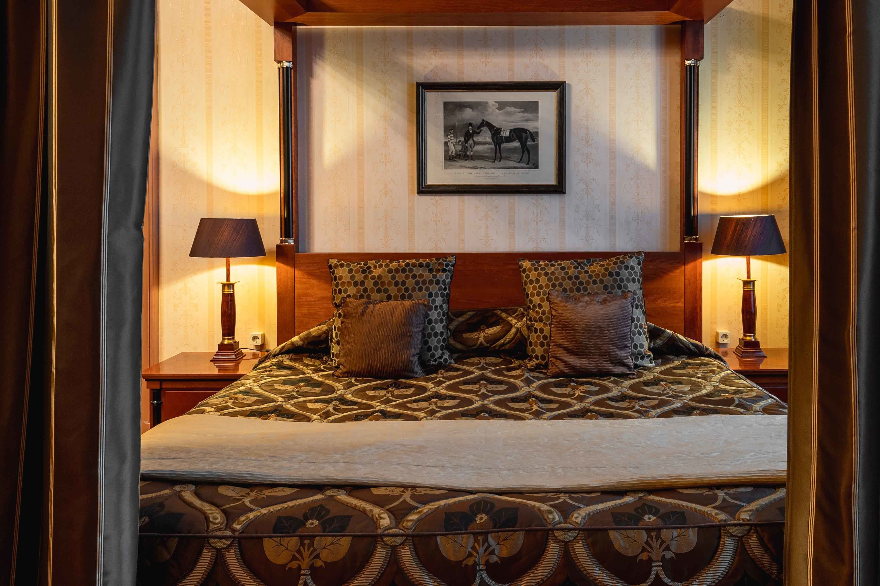 Hotelkamer met een groot bed, twee bedlampen, een fotokader aan de muur en een bedsprei met dessin.
