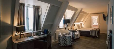 A hotel room with a desk, a bed, a chair, and a small table.