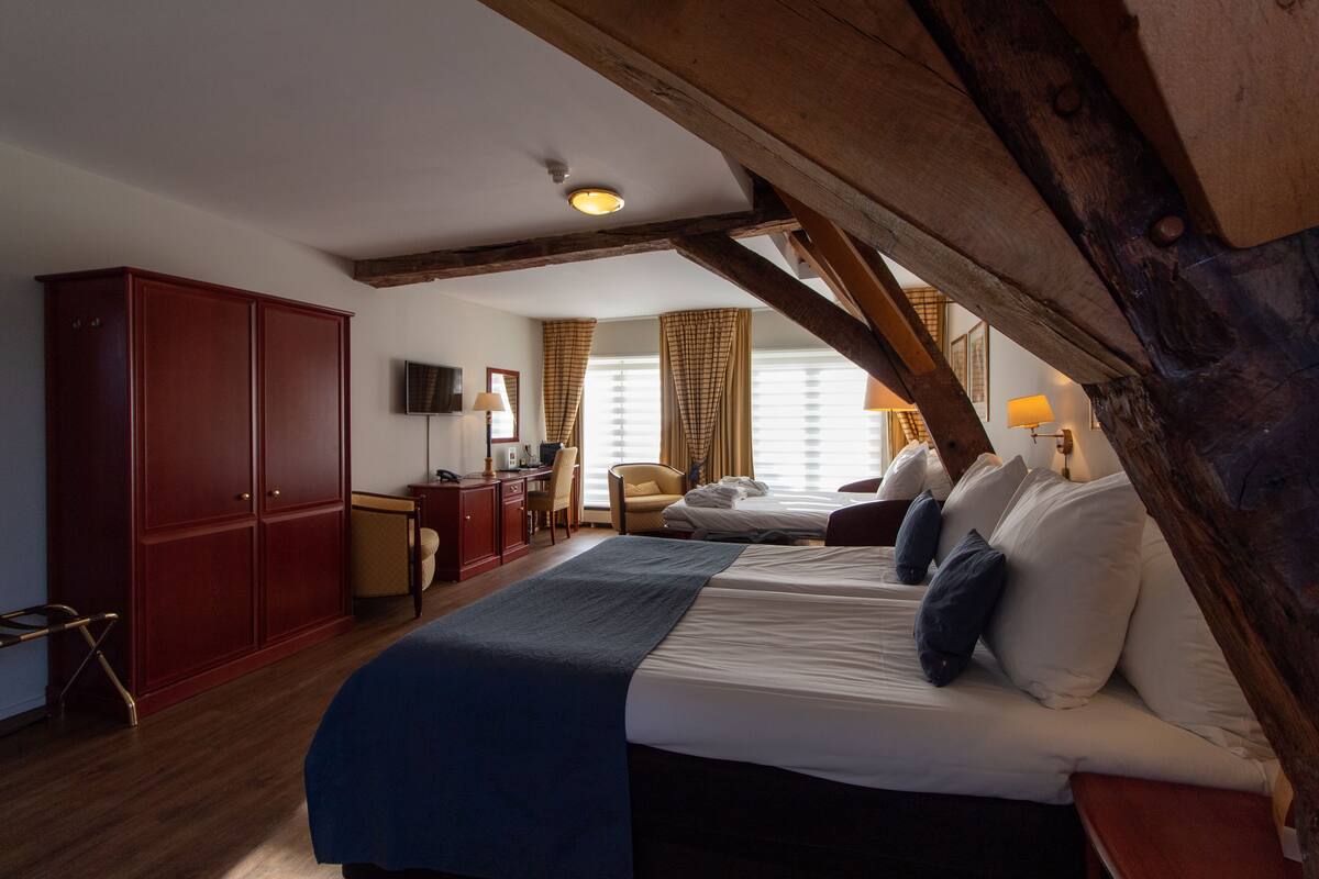 A bedroom with a large bed, a desk, a wardrobe, and a television.