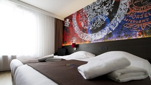 A neatly made bed with white and brown linens, a red lamp, and a colorful abstract wall art. - Bastion Hotel Maastricht Centrum (Maastricht)