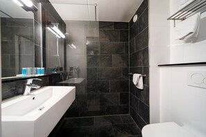A modern bathroom with a white sink, dark tiled walls, and a glass shower enclosure. - Bastion Hotel Maastricht Centrum (Maastricht)