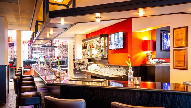 A bar area with a long counter, multiple stools, and a television mounted on the wall. - Bastion Hotel Maastricht Centrum (Maastricht)