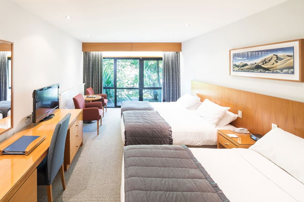 Habitación de hotel con cama, escritorio, silla, televisor y ventanas amplias.