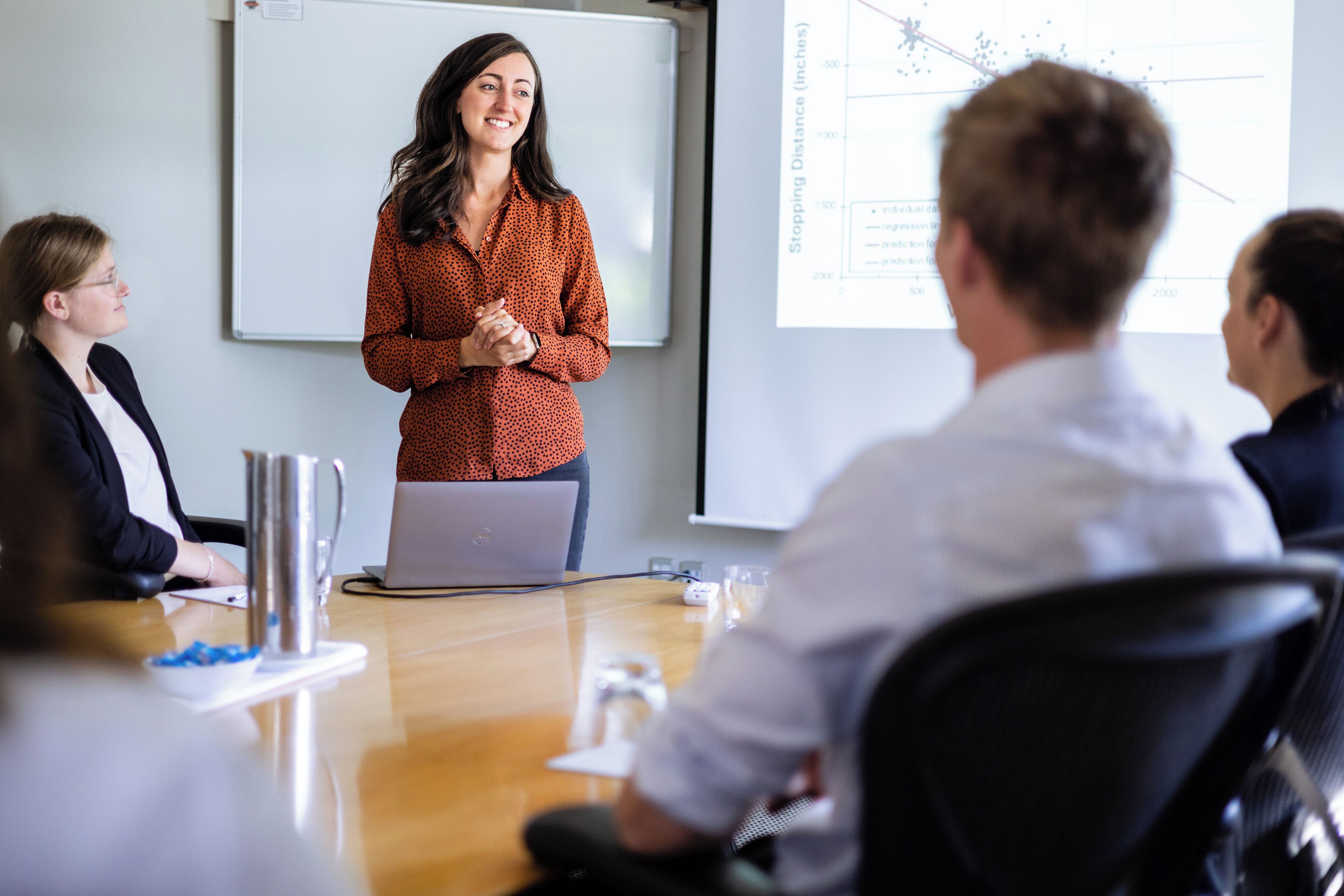 A conference room with a presentation screen, a laptop, and attendees seated around a table.