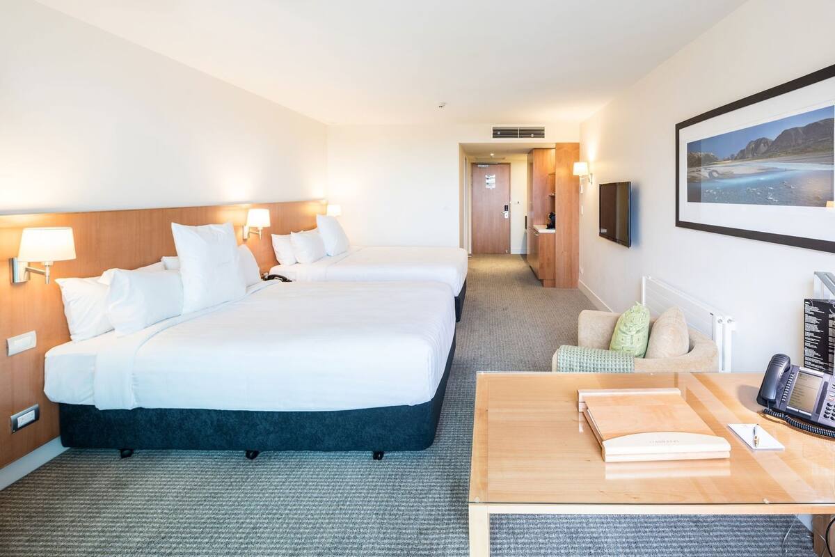 A hotel room with two beds, a desk, a chair, a TV, and a painting on the wall.